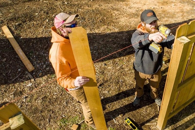 Two men working together to install a wooden fence